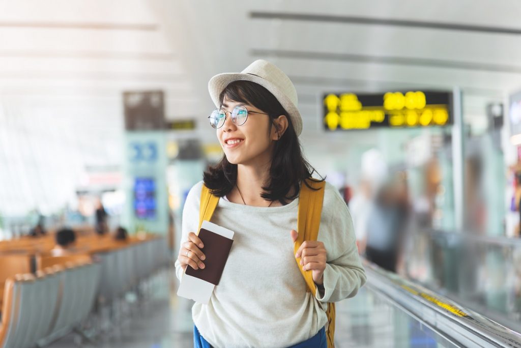 Asian woman wear glasses, hat with yellow backpack is holding fl