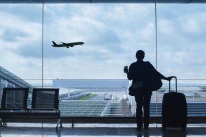 Woman holding suitcase while watching a plane take off.