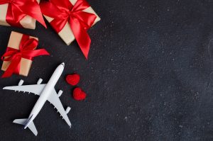A dark background with gift boxes with red bows on them, a model airplane, and two red crocheted hearts.