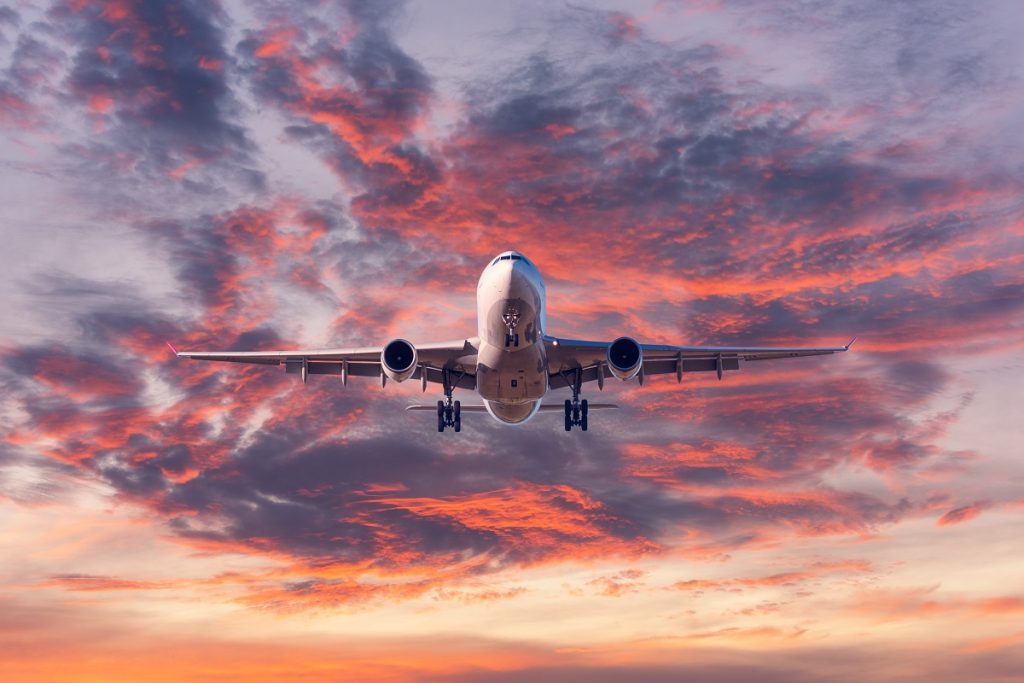 A white plane comes in for a landing with colorful clouds at sunset.