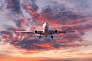 A white plane comes in for a landing with colorful clouds at sunset.
