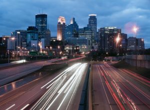 A time-lapse image of a busy highway beneath the Minneapolis skyline.