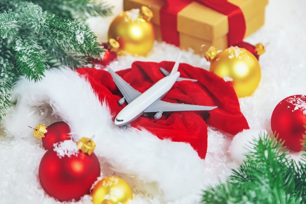 A miniature airplane resting on a Santa hat next to some ornaments, presents, and greenery
