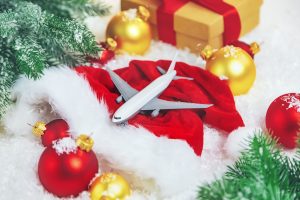 A miniature airplane resting on a Santa hat next to some ornaments, presents, and greenery